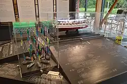 A display showing a rack of neon fishing lures and a model fishing boat in front of black and white signs