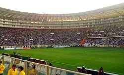 Photograph of a modern football stadium's interior; the stands are full of spectators