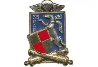 Blue Winged Rectangle with two crossed cannons reading Droit Devant topped by a red and gold shield armor