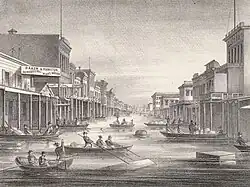 A black and white lithograph showing a flooded street in Sacramento caused by the January 1862 North American Megastorm. People are visible boating on the street.