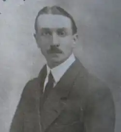 A mid-length portrait of a man of about 30 in a conservative suit and wearing a moustache, facing the camera.