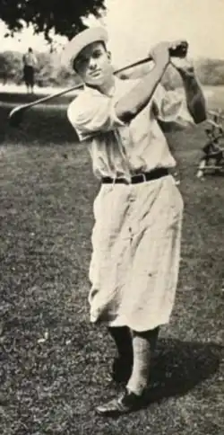 A young white man in a golf swing pose, wearing short loose trousers typical of a 1920s golf costume
