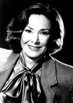 Black and white photo of a smiling woman about 50 years of age and wearing a jacket and tied-up scarf