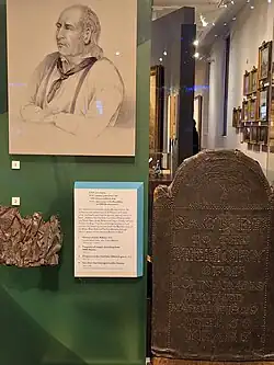 Part of the display in the National Maritime Museum in Greenwich, showing (1) the portrait of John Adams (1829) by John Alfred Vinter, after Richard Beechey; (2) Fragment of copper sheathing from HMS Bounty and (3) the original marker from John Adam's grave, 1829.