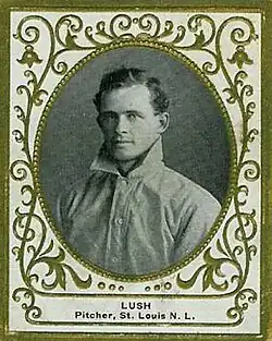 A black-and-white photograph of a curly-haired man wearing an old-style white baseball jersey with a high turned-up collar
