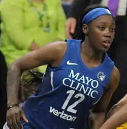 Waist high portrait of young woman running to the right wearing navy basketball uniform and blue headband