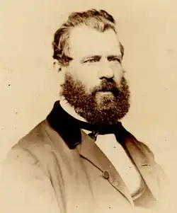 Sepia photo of Turcotte, half-profile head and shoulders; dark hair and beard, wearing mid-Victorian business suit