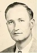 White male with dark hair in a tan suit