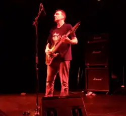 Justin Broadrick playing guitar on a red-tinted stage