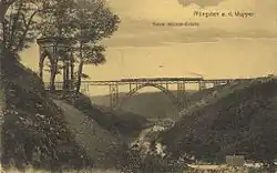 Black and white view of steel arch bridge crossing a forested valley. A steam train is crossing the bridge