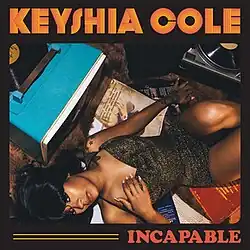 A photograph of Keyshia Cole laying down on a hardwood floor with two record players in front of her.