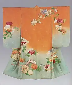 A peach- and light blue-grey coloured kimono with medium-length sleeves viewed from the back. It has a single crest just below the collar at the back, and is lined in light pink. The kimono is woven with an abstract design of bamboo shoots, with the fabric beginning as a light blue-grey on the hem before graduating into a strong peach colour at the top. The kimono is decorated with a hand-painted design of flowers and plants.