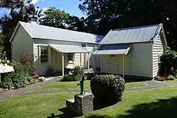 A view of two small white buildings with a hand water pump