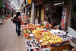 A female customer browsing a fruit shop. Banana and grapes are displayed on the front.