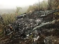 Remains of a helicopter, with the environment showing signs of fire. The only part remaining of the aircraft is the tail