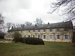 Photograph of the main building of the Colonie, Condé-sur-Vesgre. It is a long symmetrical one-storey building with large regular windows, six on each side of the door. In front of it is a small grassy area with bushes and a few trees.