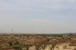 Image of small flat mountains in Ibrohamane. The ground is red and there is sparse foliage. There are some settlements as well.