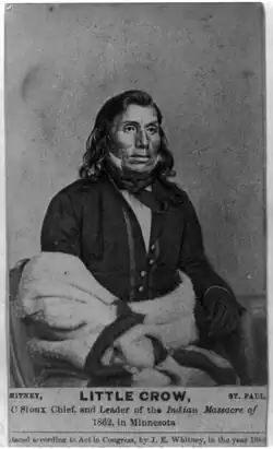 A photograph of a Native American man seated, wearing a suit