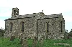 A small, simple stone church. On the left is the nave with a bellcote at the far end, and on the right a smaller chancel