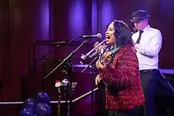 Lucy Kalantari performing live on stage, singing into a microphone.