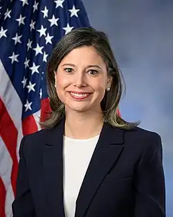 Official House portrait of Goodlander smiling in front of the U.S. flag, wearing a black jacket and white shirt.