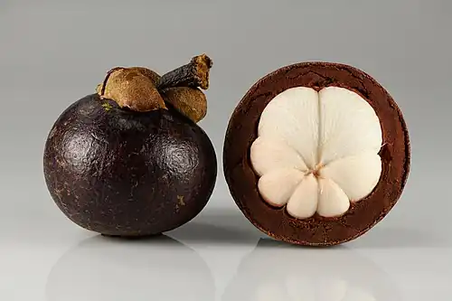 Photograph of a whole mangosteen fruit, and one partially peeled to show the horizontal cross-section which reveals the white internal flesh divided into seven sections.