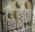 Sandstone bas-relief tombstone of Roman family. There are three figures: a boy, a mother, and a father. They are wearing Roman clothing and hairstyles.