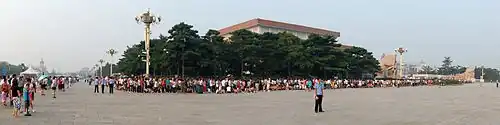 A large mausoleum in the middle of a public square, surrounded by a long line of people, as they wait to enter