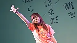 A smiling, waving Mari Okada