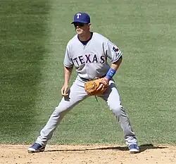 Baseball player in an athletic stance. He is wearing a blue baseball cap inscribed with a "T", and his jersey reads "TEXAS" across the front.