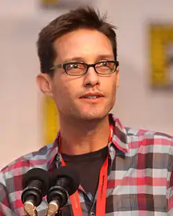 A closeup of a man. He wears dark-framed glasses.