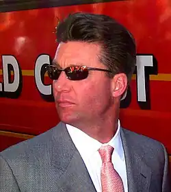 A man wearing sunglasses and a gray suit with a patterned red tie looking over his right shoulder