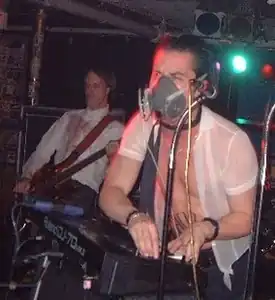 A singer, Mike Patton, performing in an elastomeric respirator (but without its filter cartridges) in 2002. Note microphone.