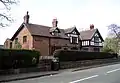 A brick and sandstone house near a road, with two gables and a dormer window, all timber framed.