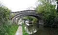 The bridge crosses the canal with a wide footpath on the left and long boats visible through the arch.