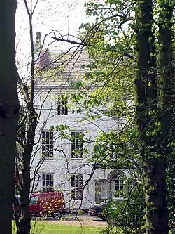 Photograph of the three-storey hall, painted white, framed by trees