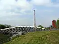 A metal swing bridge on the left over the canal, a metal pylon in the middle and brick support buildings on the right.