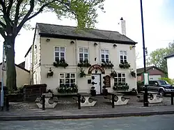 A cream-coloured public house with window boxes in front of which are picnic-type tables.
