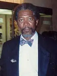 An African American man with a beard and short hair, both a mix of white and grey, and wearing an earring in each ear: He is smiling towards the camera.