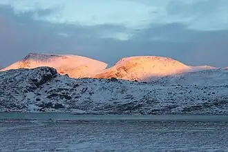 Snow-covered mountains whose peaks are bathed in an orange glow