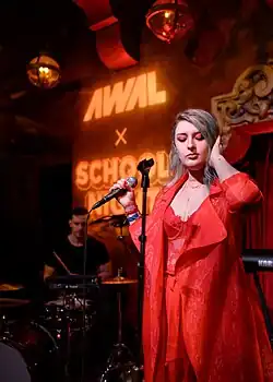 Mothica in a red outfit with shoulder-length hair holding a microphone on a stage
