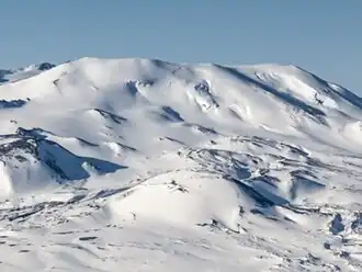 A flat-topped, snow-covered mountain overlooking a much smaller, snow-covered, cone-shaped hill