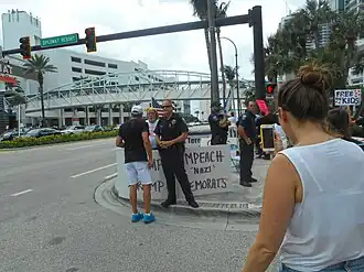 Counter-protester with "Gays for Trump" and "Impeach Nazi Democrats" signs confronted by a protester in Hollywood, Florida