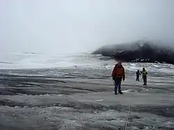 Three climbers standing on a dark glacier with a black mountain in the right background
