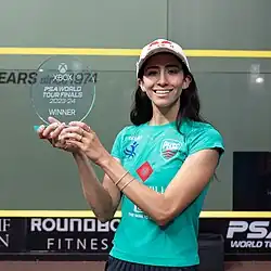 A portrait photo of Nouran Gohar where she holds up the winner’s trophy