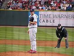 A man in a white baseball uniform and red baseball cap wearing a black baseball glove on his left hand
