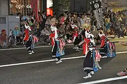 Masked men with swords and traditional dress dancing on a street.