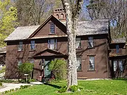 A dark brown colonial frame house with wooden shingles.