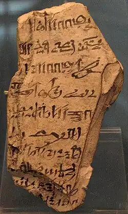 A light-colored stone fragment with hieratic handwriting in black ink scrawled on its surface