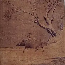A boy riding an ox and a tree.
